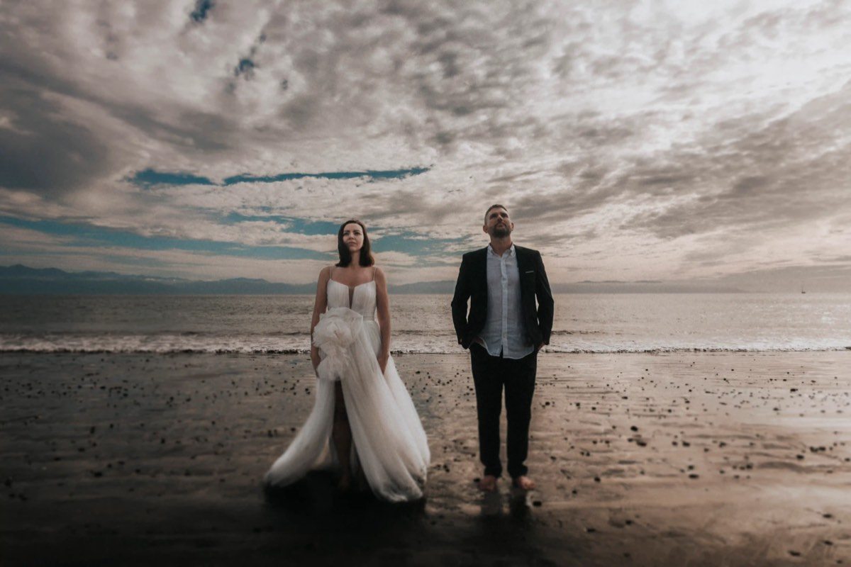 Novios caminando descalzos por la playa al atardecer
