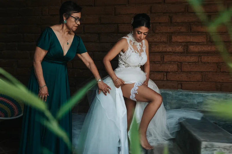 La novia acomodándose el liguero mientras su madre la acompaña en los preparativos