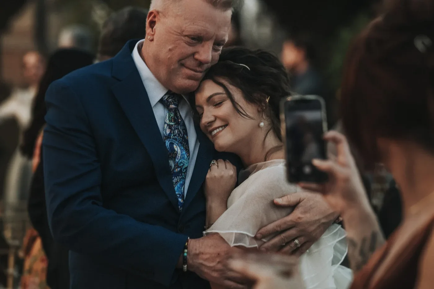 El papá de Laura abrazándola después de la ceremonia, mientras alguien toma una foto con el celular