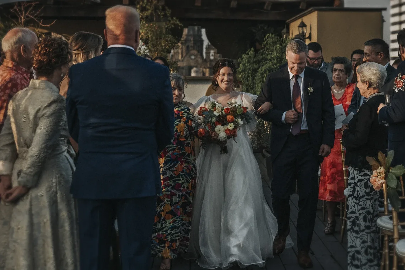 Laura entrando a su ceremonia del brazo de su papá, con los invitados de pie
