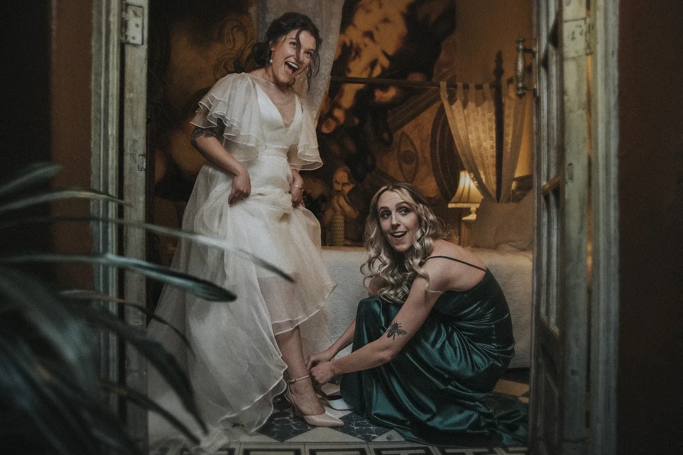 Laura riendo mientras se pone los zapatos antes de la boda, con ayuda de una amiga