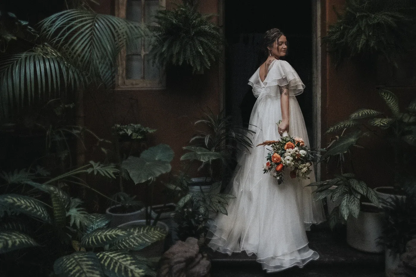 Laura, la novia, de espaldas entre plantas con su ramo de flores en Casa Pedro Loza