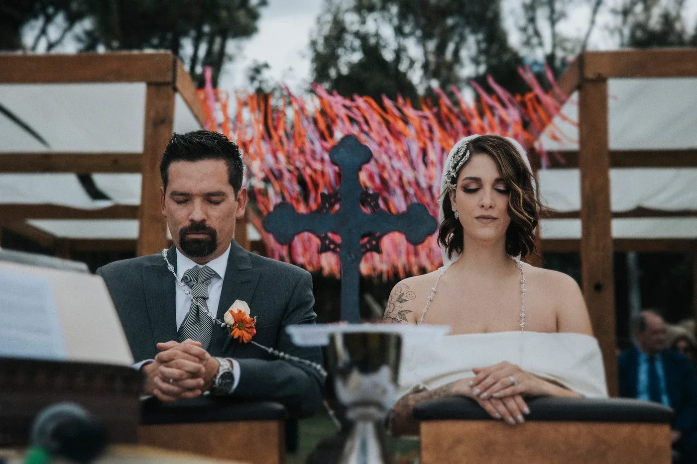 Lucía e Iván con los ojos cerrados durante un momento de la ceremonia religiosa, con una cruz de fondo