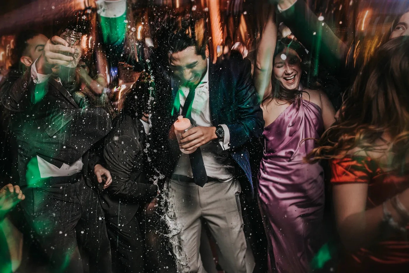 Invitados bailando y salpicando agua durante la fiesta de la boda, con luces de colores