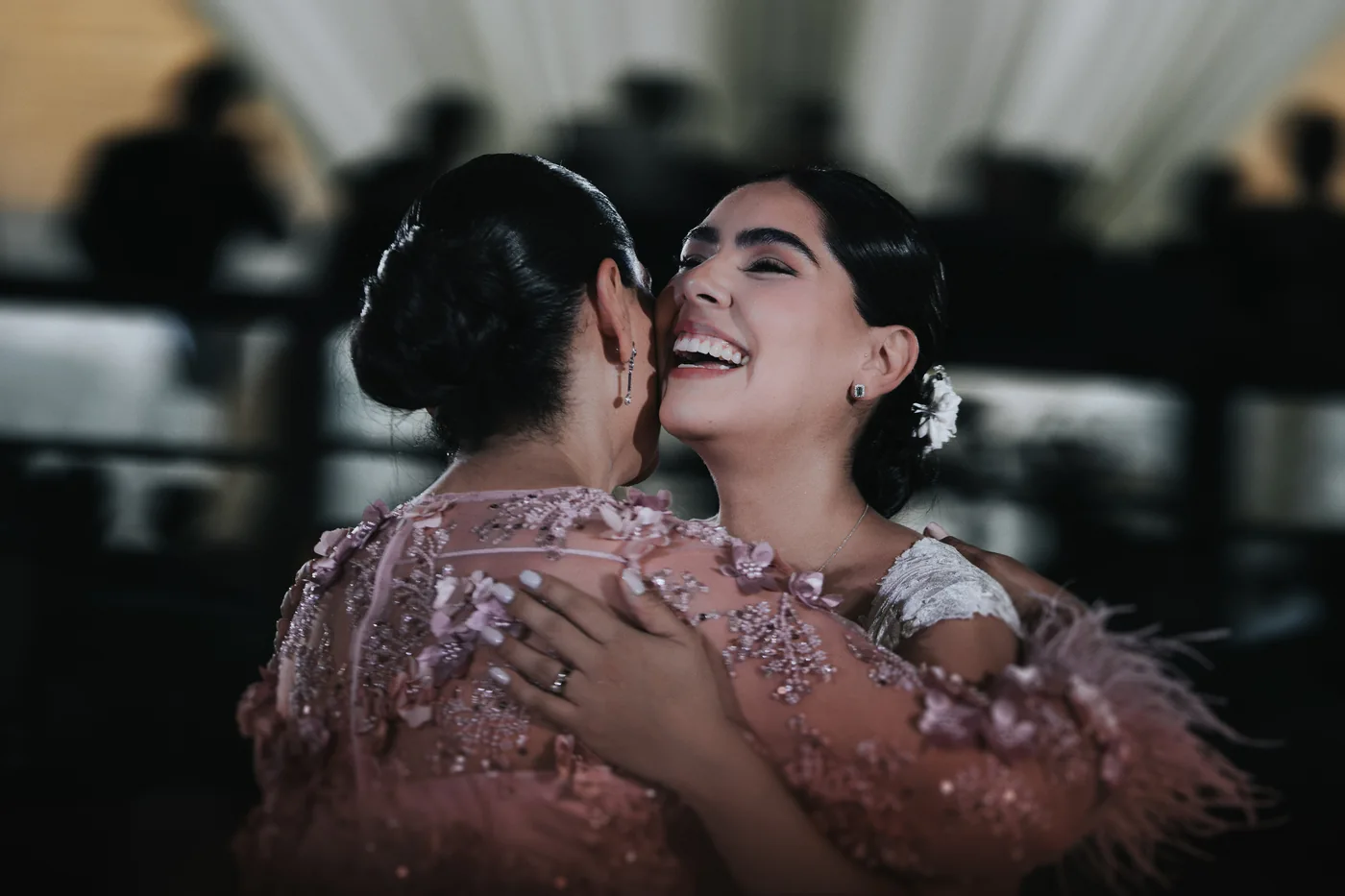 Marla ríe abrazada a su mamá, de vestido rosa con plumas, en la recepción