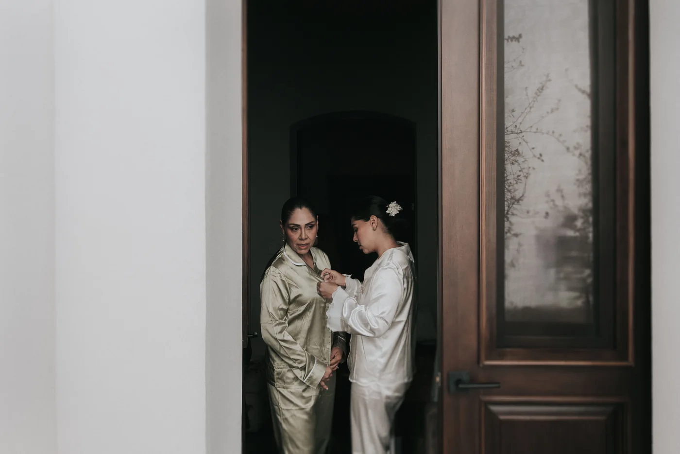 Marla le acomoda la pijama a su mamá en el marco de una puerta, durante los preparativos