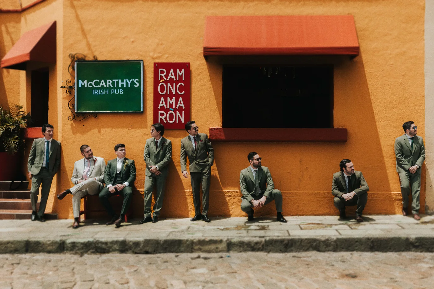 Los padrinos de Edy, de traje verde, recargados en una pared naranja bajo el letrero de un pub irlandés en el centro de Oaxaca