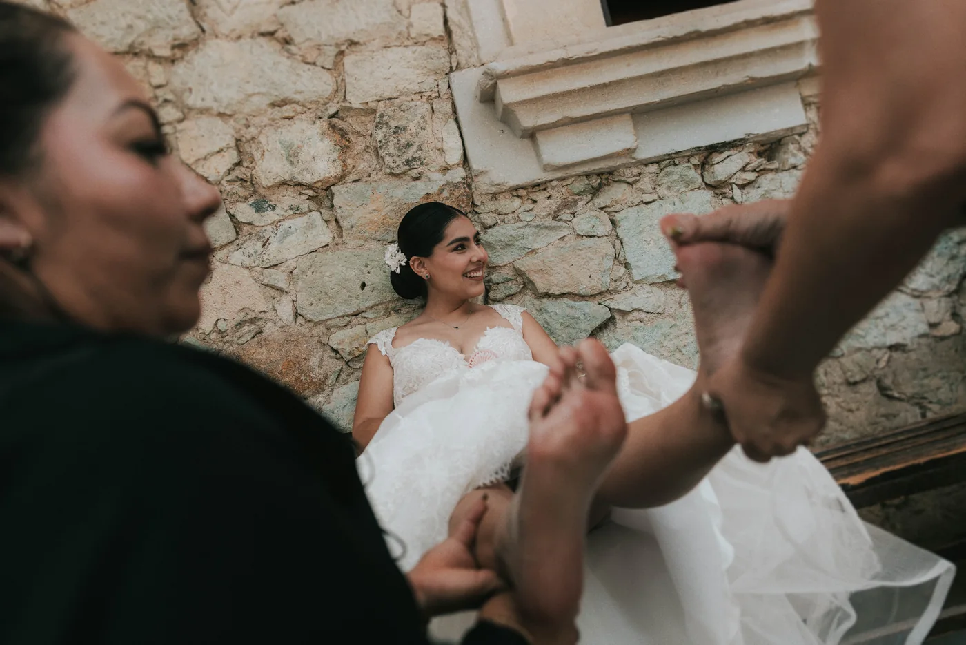 Marla, descalza y sentada contra un muro de piedra, recibe un masaje en los pies del equipo de su wedding planner