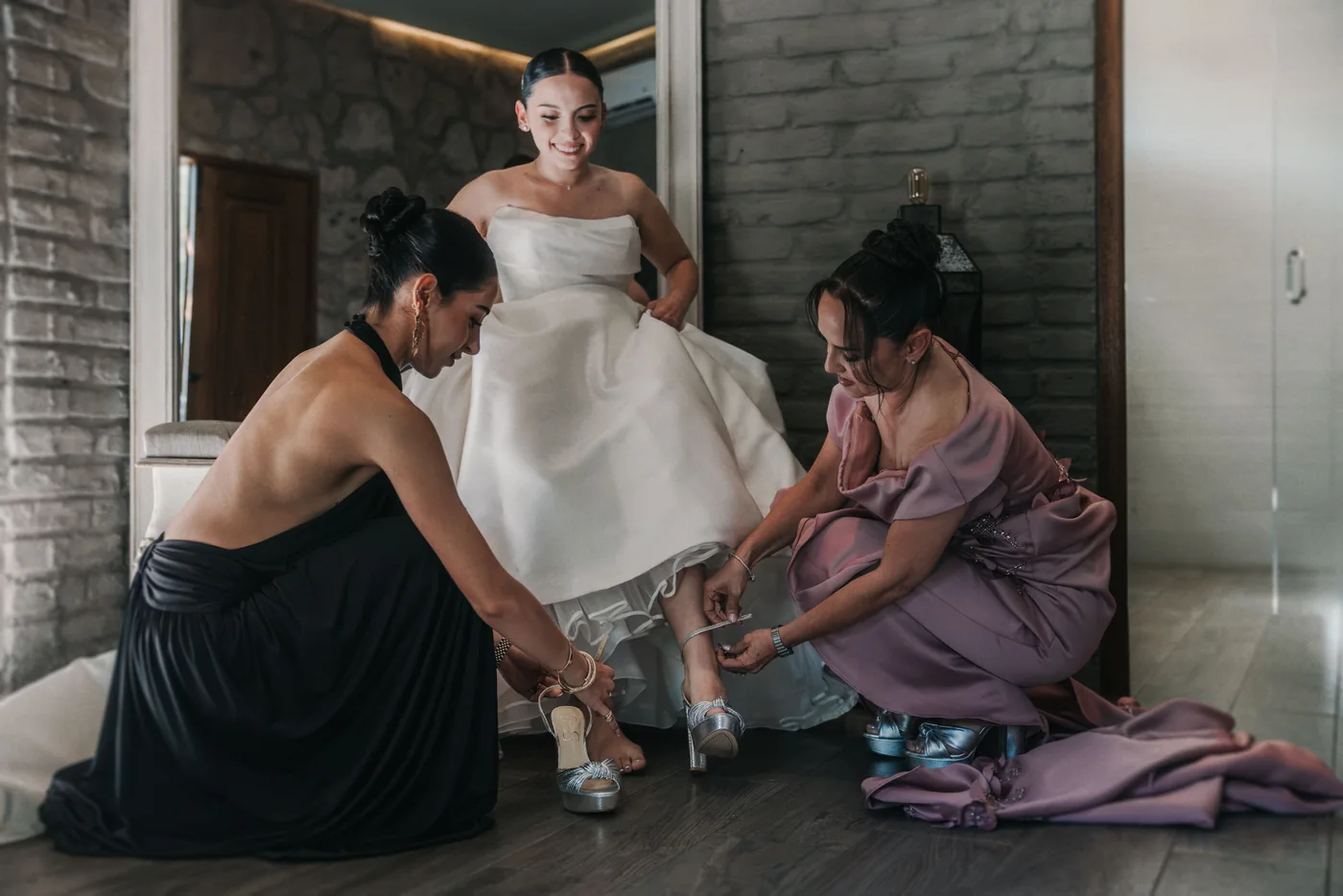 La mamá y la prima de Sofi le abrochan las zapatillas plateadas mientras ella sonríe