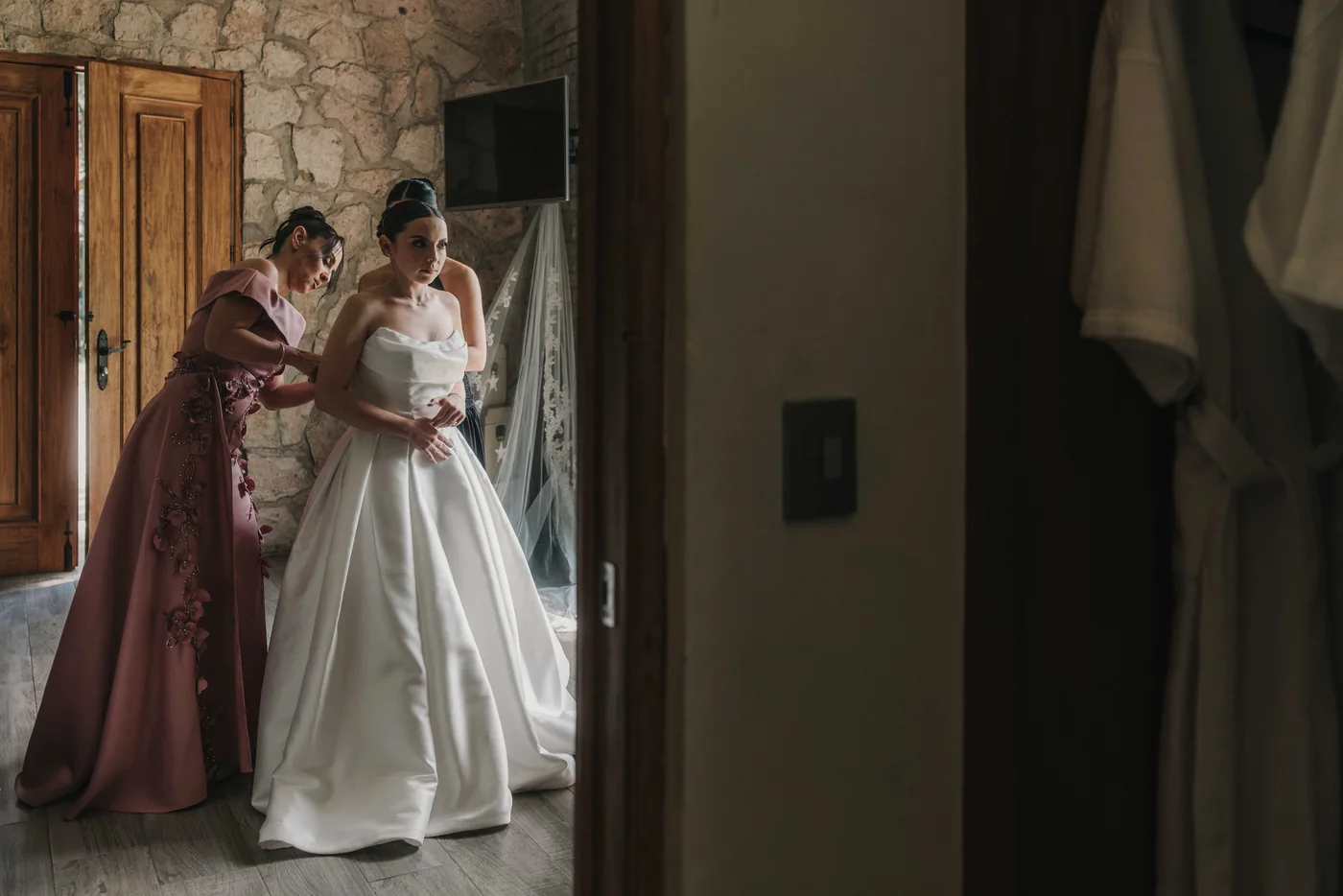 La mamá de Sofi le ajusta el vestido de novia, vistas a través de una puerta