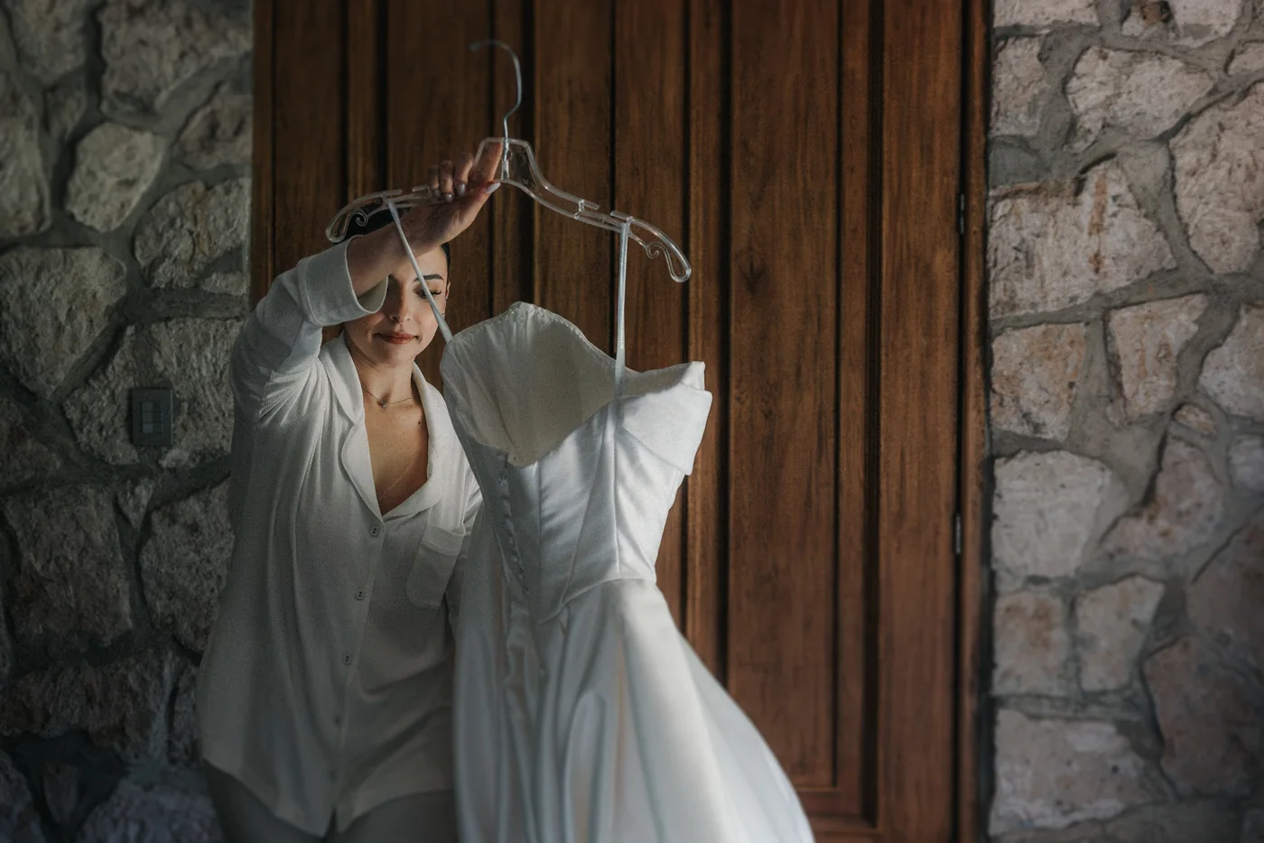 Sofi sostiene su vestido de novia colgado de la percha frente a una puerta de madera