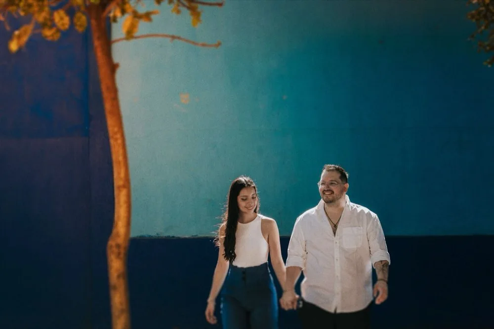 Pareja tomada de la mano frente a un muro azul intenso