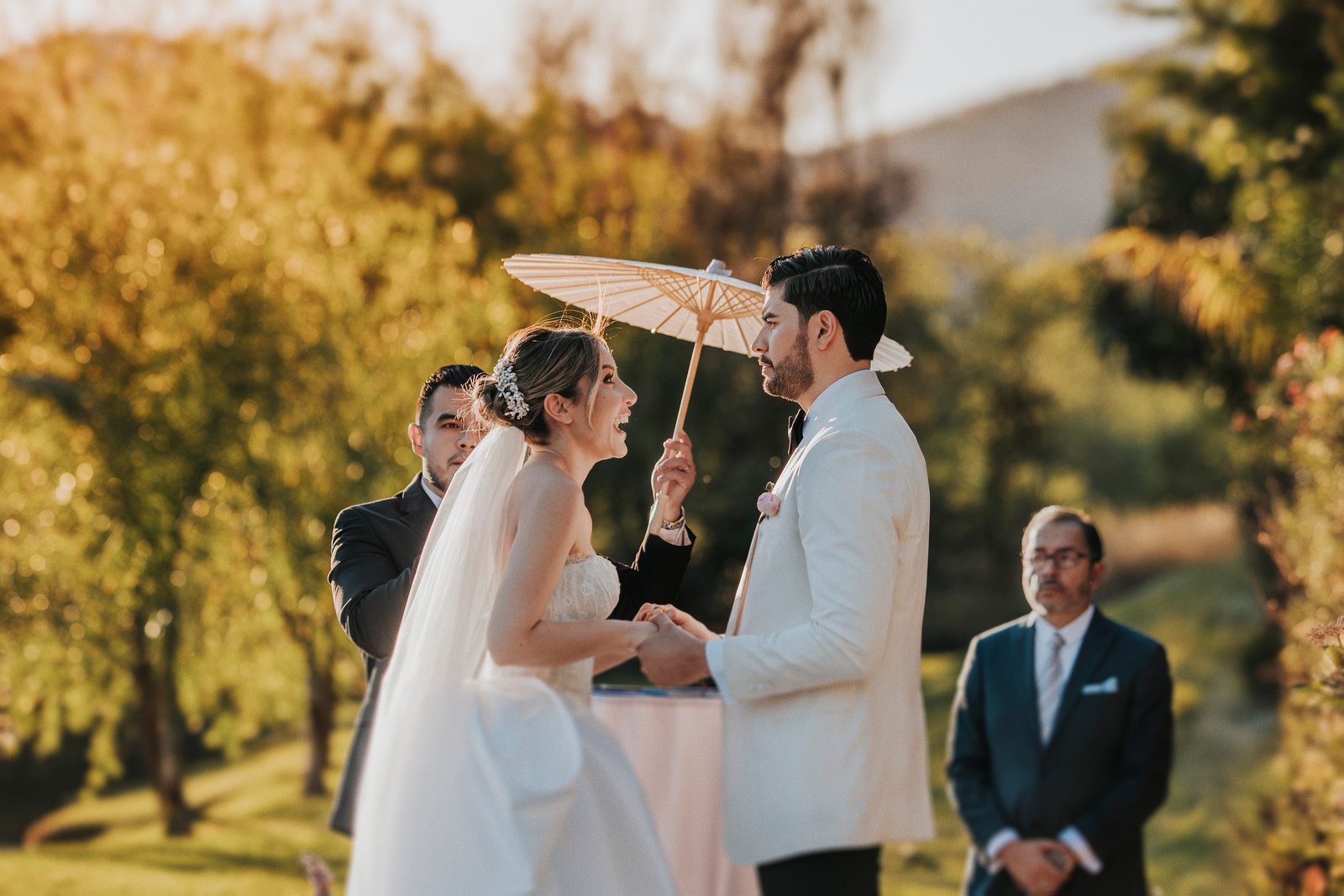 Novios tomados de la mano durante la ceremonia, con la luz dorada del atardecer