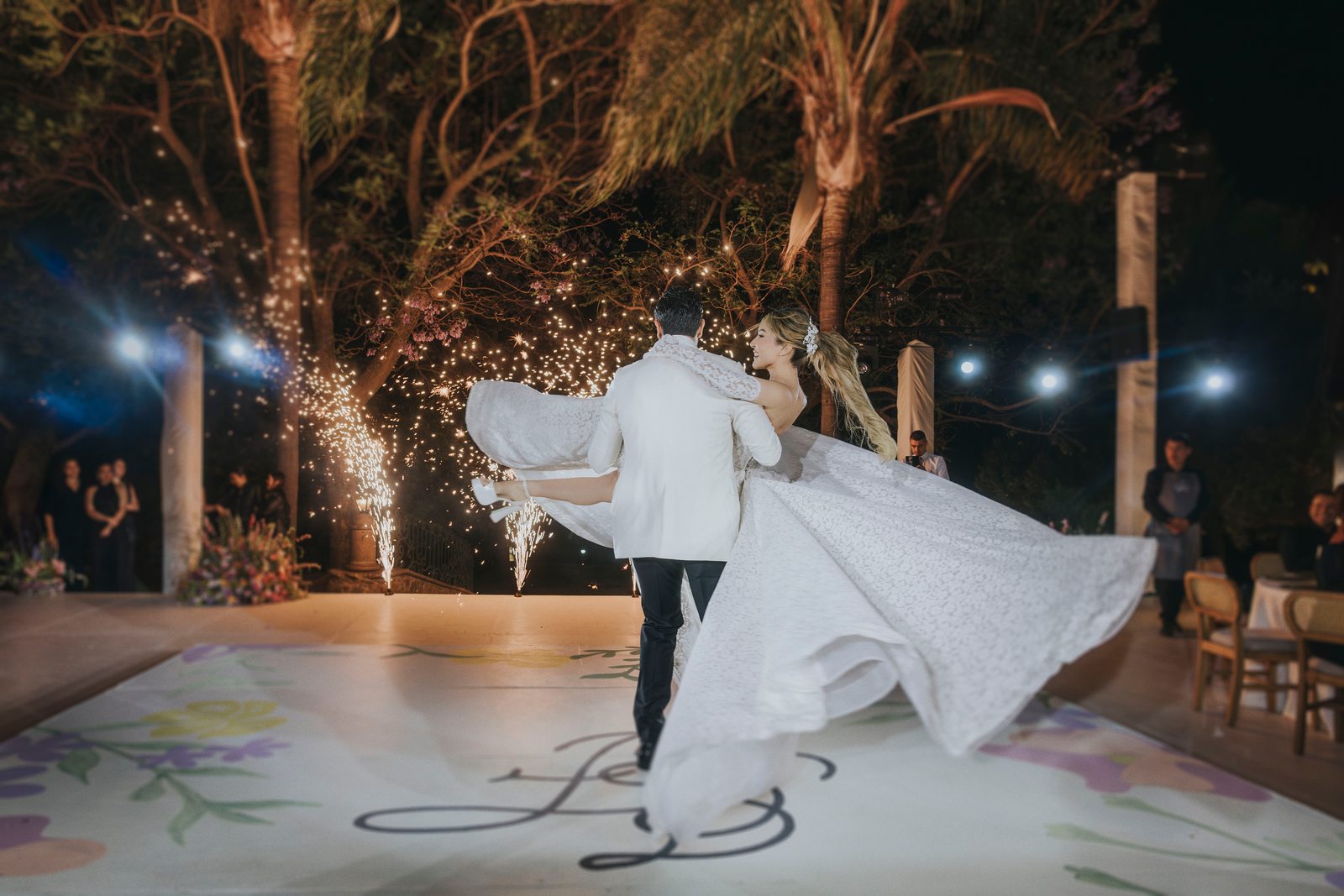 Primer baile de los novios de noche, con chispas frías sobre una pista pintada a mano