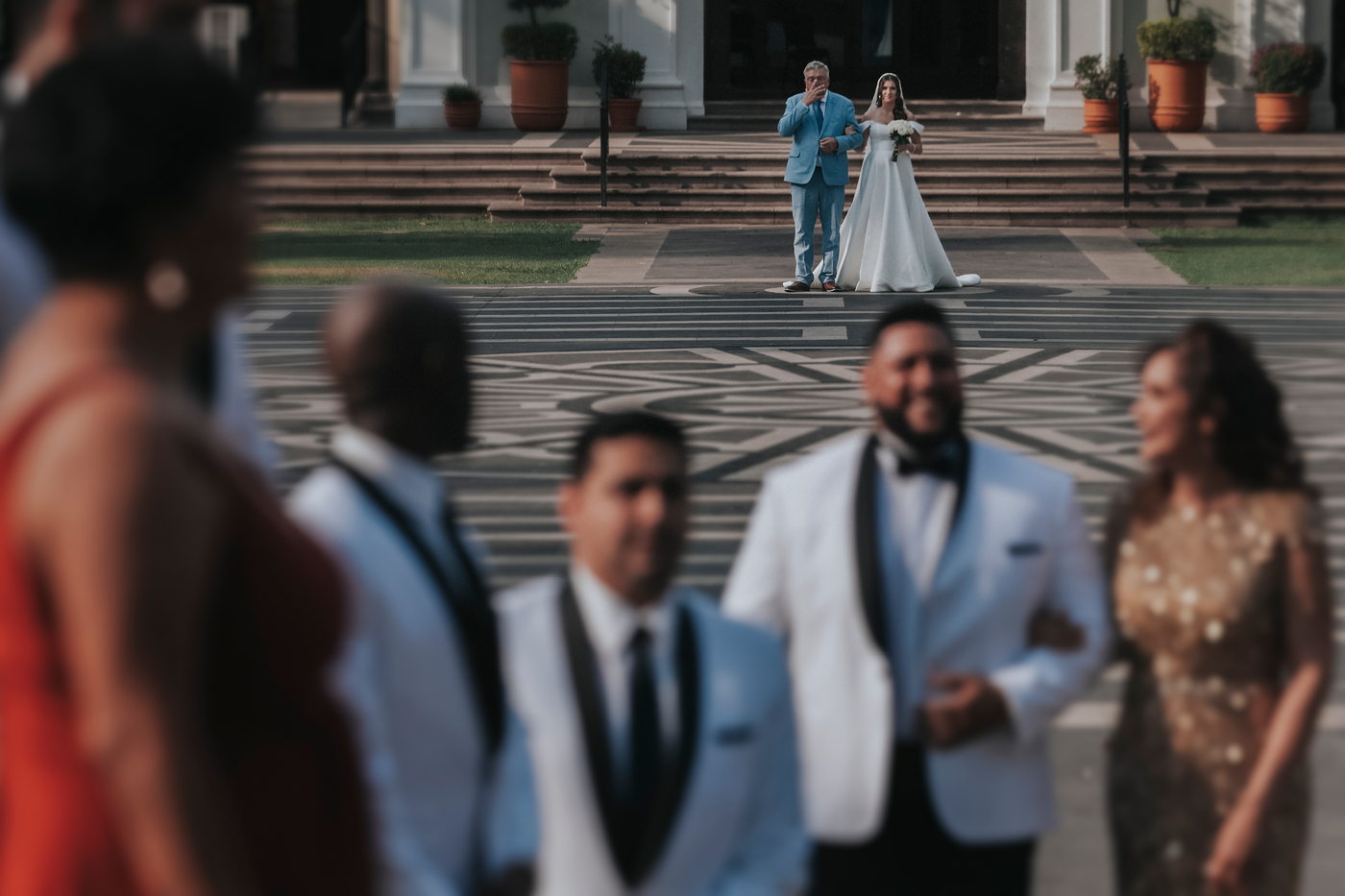 La novia y su padre al fondo de la plaza mientras los invitados esperan en primer plano