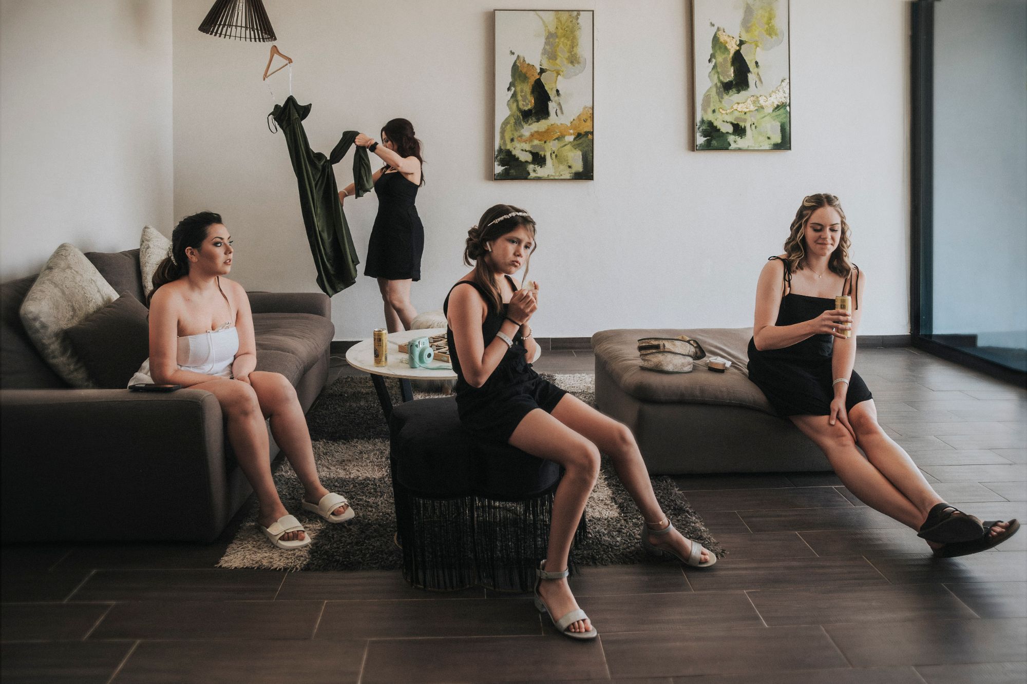 Cuatro mujeres en una sala durante los preparativos de la boda, cada una en lo suyo: una cuelga un vestido verde, otra mira a lo lejos y una niña con diadema come mirando a un lado