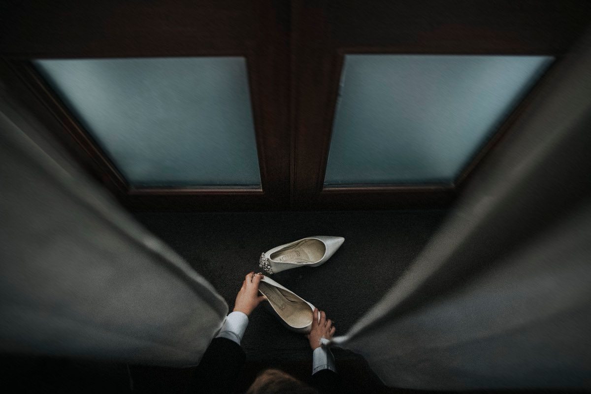 Detalle de zapatos de novia sostenidos a la entrada de una puerta